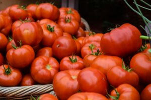 Close-up photograph showing a large quantity of fresh, ripe red tomatoes stacked in woven wicker baskets at a market or distribution center. Tomato Production in the United States: Structural Constraints Persist