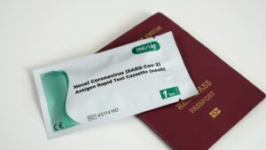 Primer plano de un sobre de prueba rápida de antígenos para COVID-19, de la marca REALy, colocado sobre un pasaporte de color burdeos. El sobre está sellado y el pasaporte cerrado, ambos sobre una superficie blanca.