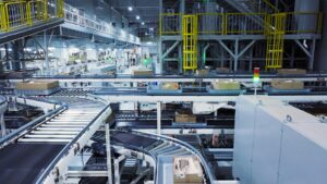 Vista panorámica de un centro de distribución totalmente automatizado, con sistemas de cintas transportadoras de rodillos, estructuras metálicas multinivel y cajas recorriendo las líneas de clasificación logística.