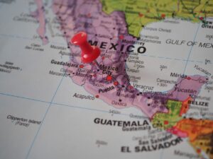 Primeiro plano de um mapa físico do México com um alfinete vermelho fixado na região central, perto da Cidade do México, mostrando os nomes das principais cidades e da costa.