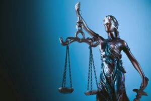 Escultura de bronce de la Dama de la Justicia sosteniendo una balanza con cadenas y una espada sobre un fondo de tonos azules con iluminación lateral que resalta su silueta. Comprender las reclamaciones por muerte injusta y las opciones legales.
