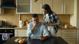 Pareja preocupada revisando una factura en una cocina doméstica, representando la necesidad de reorganizar deudas de alta tasa y buscar soluciones financieras para bajar la cuota mensual.