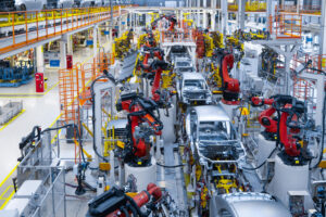 Línea de ensamblaje automotriz altamente automatizada con múltiples brazos robóticos industriales rojos trabajando en las carrocerías de vehículos dentro de una moderna planta de manufactura en América del Norte. Manual de auditoría de origen en el T-MEC: la propuesta de la AMIA a la USITC.