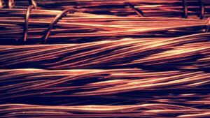 Primeiro plano detalhado de fios grossos e cabos de cobre enrolados industrialmente com reflexos metálicos avermelhados, representando a produção, a exportação e a força do setor de mineração na economia chilena.