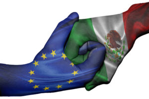 Deux mains se serrant fermement sur un fond blanc : l’une arbore le drapeau de l’Union européenne et l’autre les couleurs et les armoiries nationales du drapeau mexicain.