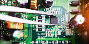 Plano en acercamiento de una placa de circuito impreso verde donde unas pinzas de precisión colocan cuidadosamente un microchip electrónico rodeado de transistores, condensadores y resistencias. Mercado internacional más importante de Jabil: México supera a Malasia y China.