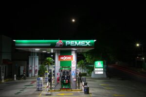 Photo nocturne d’une station-service PEMEX avec un éclairage vert et une signalisation NEXUM, montrant des pompes à essence et une pleine lune sur fond sombre. Le SIRACP améliorera la logistique du secteur des hydrocarbures au Mexique.