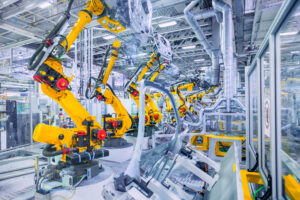 Una hilera de brazos robóticos industriales de color amarillo trabajando en una línea de ensamblaje automatizada dentro de una moderna planta de manufactura y producción de componentes. Empleos de Key Tronic en México: la plantilla baja 40% por automatización.